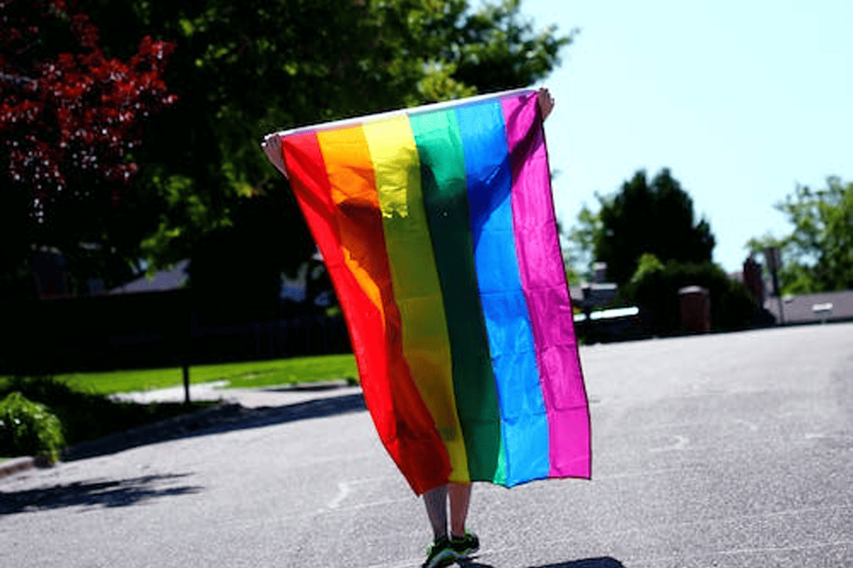 Person walking holding rainbow colored pride flag, June 4, 2019. (Photo/Alexander Grey, Pexels)